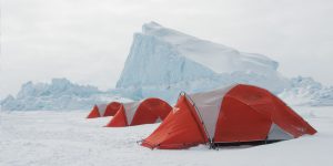 Three tents set up for adventurers on the frozen ocean next to icebergs that have wedged themselves in the ice in Nunavut.