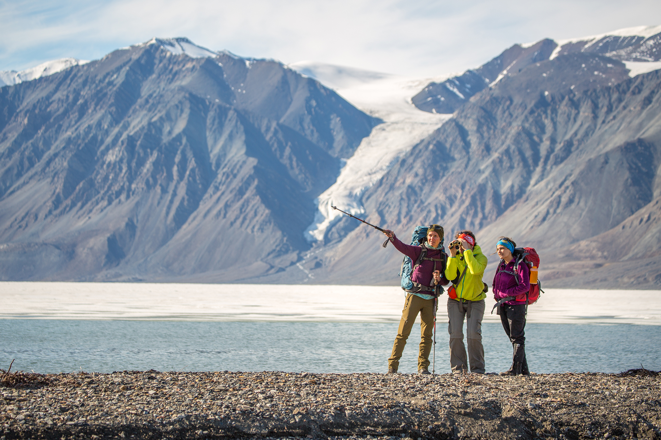 Three hikers in the spring near the bay with a glacier in the background in Nunavut.