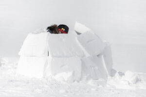 Person making a small igloo with blocks of ice on the snow in Nunavut.