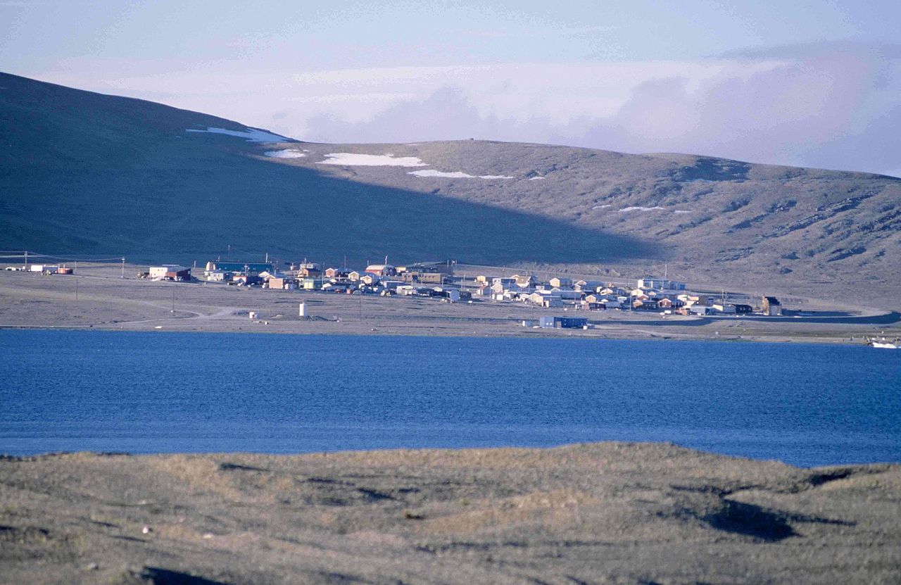 Resolute Bay, Nunavut. Landscape photograph of the community, with the tundra in the foreground and mountains in the background. The weather is nice and sunny.