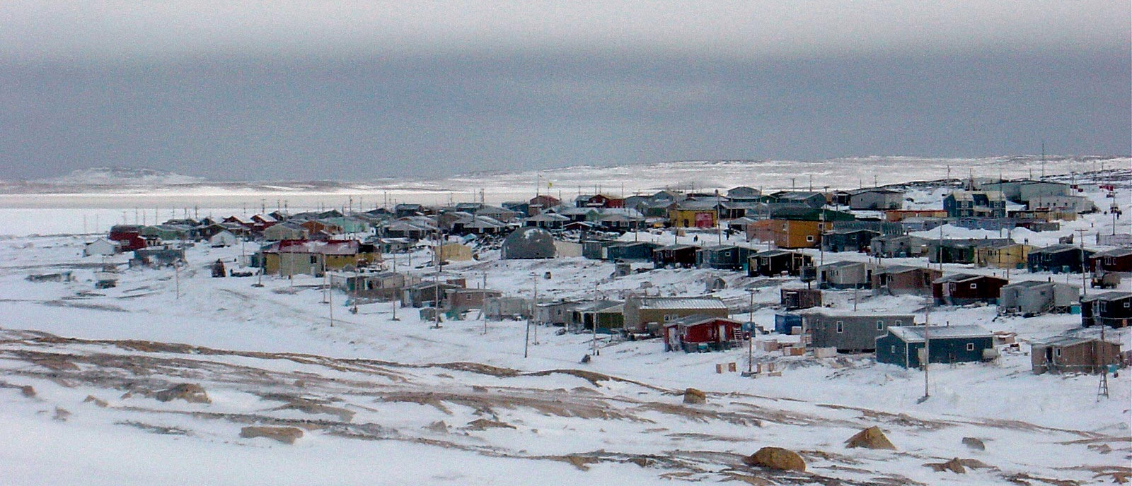 Sanikiluaq, a small community in Nunavut. Photograph taken during winter with windswept and exposed tundra in the foreground.