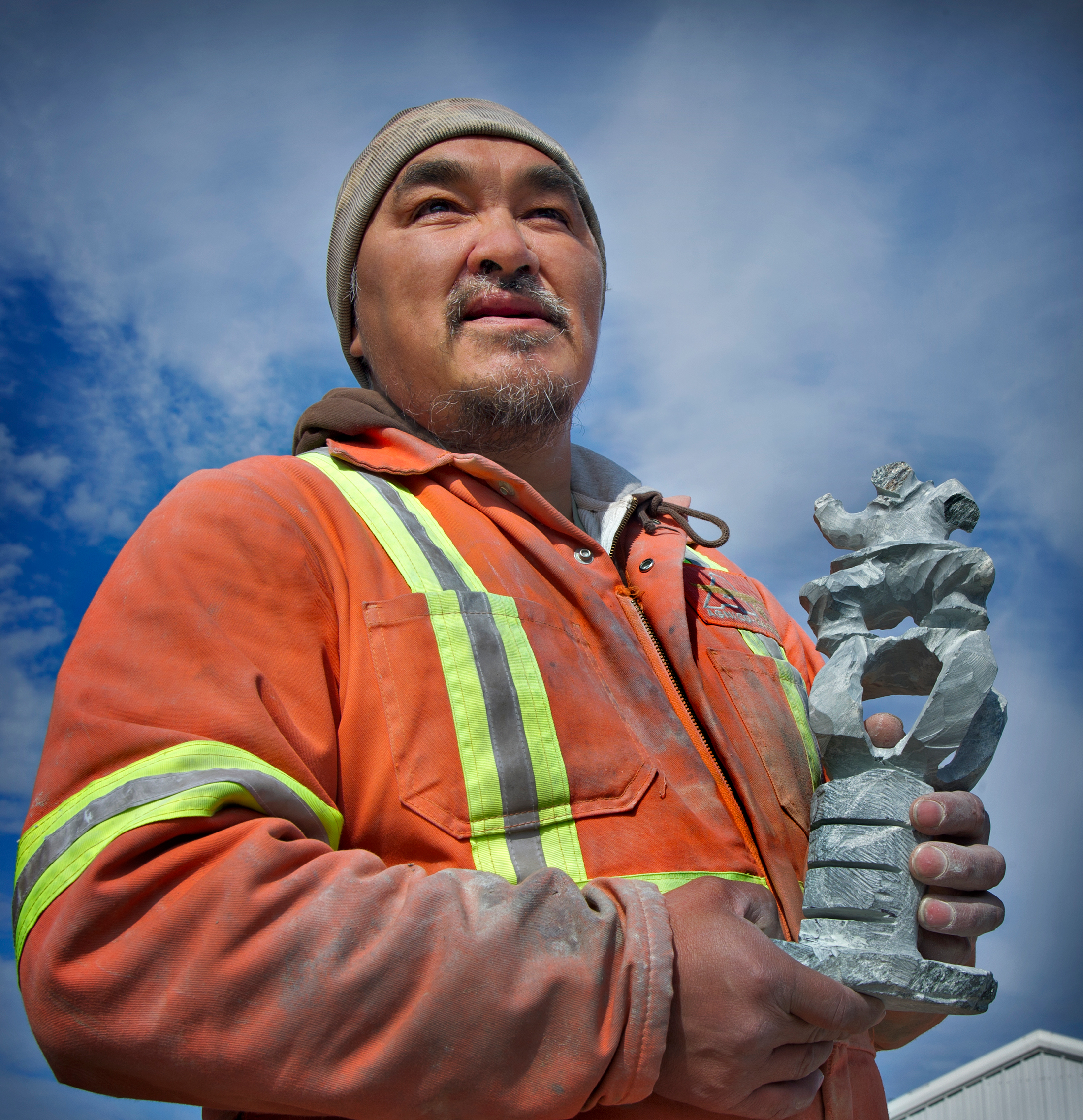 Image of Inuit man stood outdoors with one of his limestone carvings in Nunavut.
